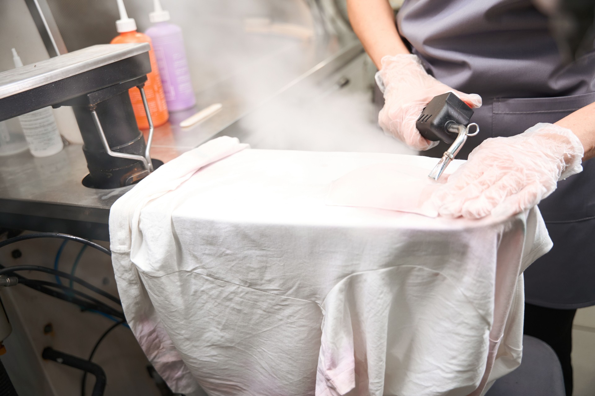 Worker of dry-cleaning service doing pre treatment, using steam gun